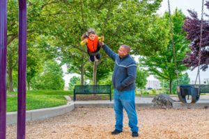 man pushing young boy on swings at Stone Creek Community Park playground